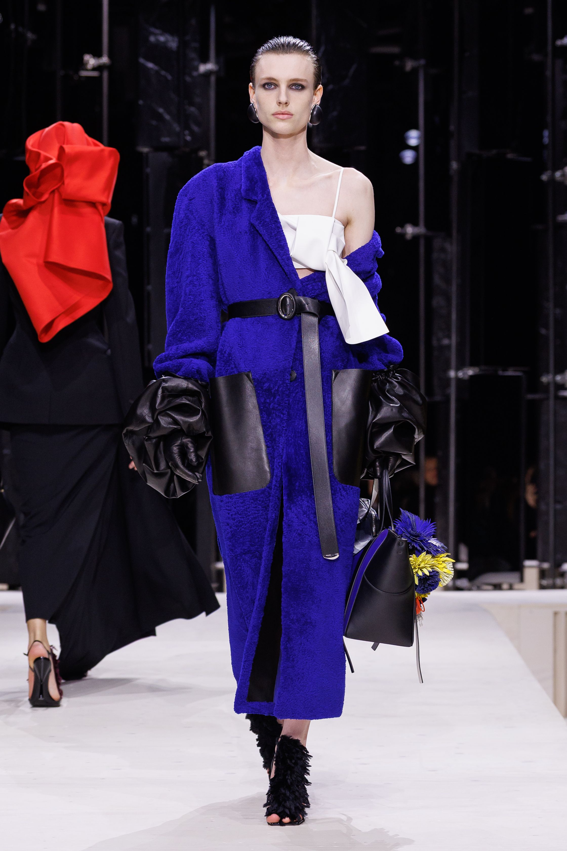 Givenchy 2026秋冬在现代建筑空间中呈现一场充满戏剧性的时装叙事：雕塑式西装、亮色斗篷、结构礼服与夸张装饰共同构建品牌标志性的高级时装气质。蓝色、红色与黄色的高饱和色彩与黑白经典形成鲜明对比，服装通过立体剪裁与夸张廓形展现出强烈视觉张力。整场系列在优雅与戏剧之间取得平衡，展现现代高级时装的力量-顽石频道趋势研究